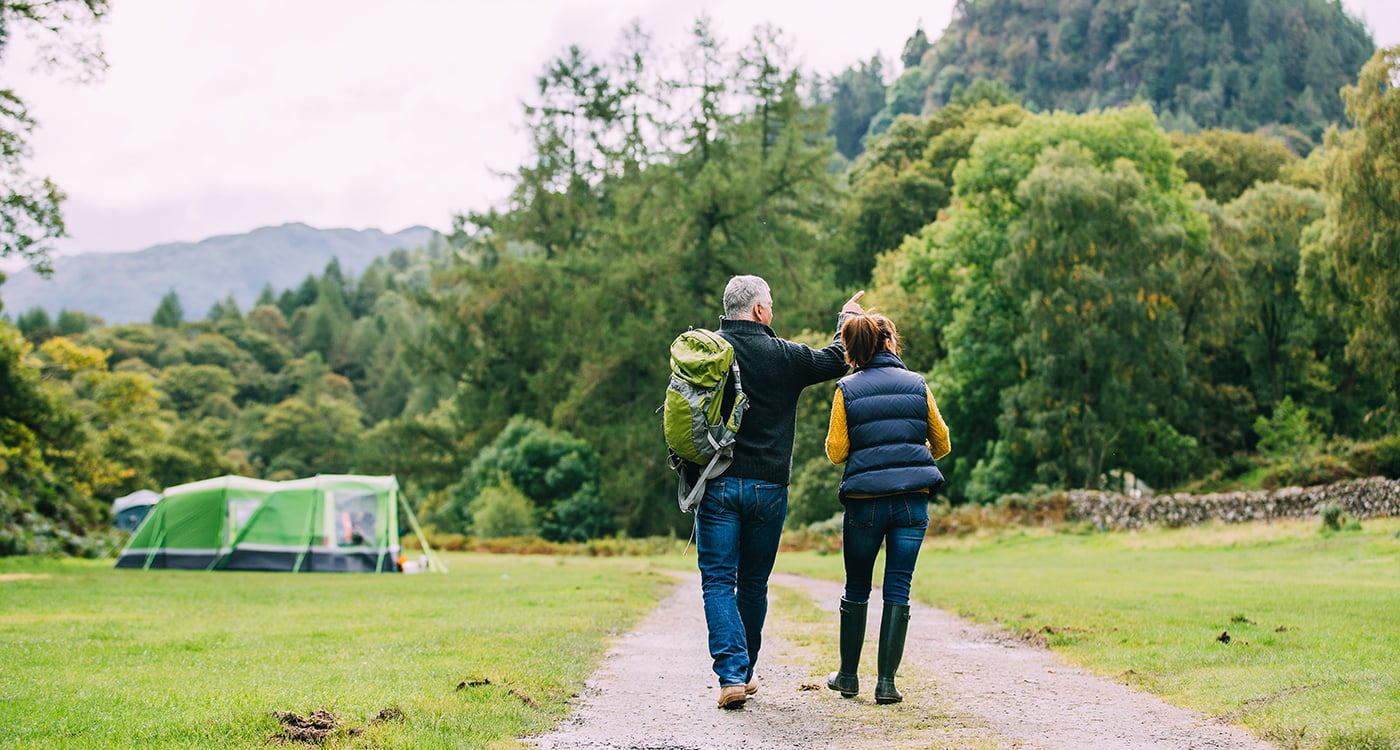 A man and a woman walking outdoors towards a campsite