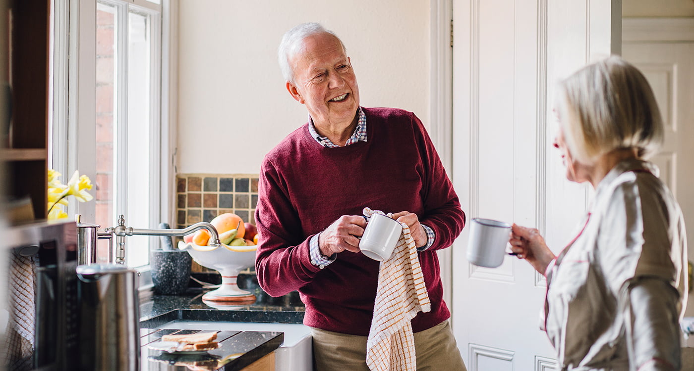an older man talking to a woman while wiping dishes in the kitchen