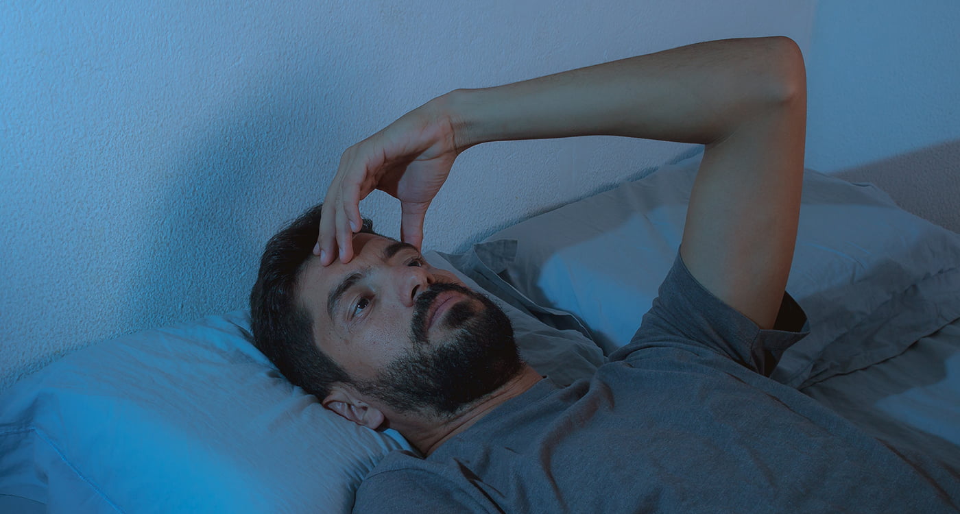 a man laying in bed with his hand on his forehead